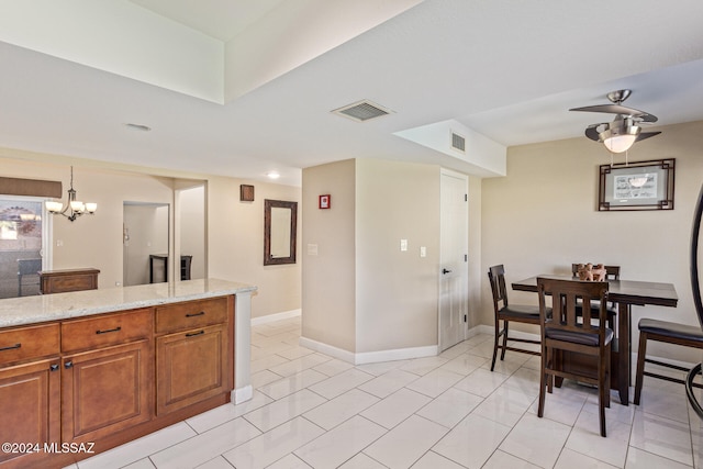 kitchen featuring pendant lighting, light stone counters, light tile patterned floors, and ceiling fan with notable chandelier