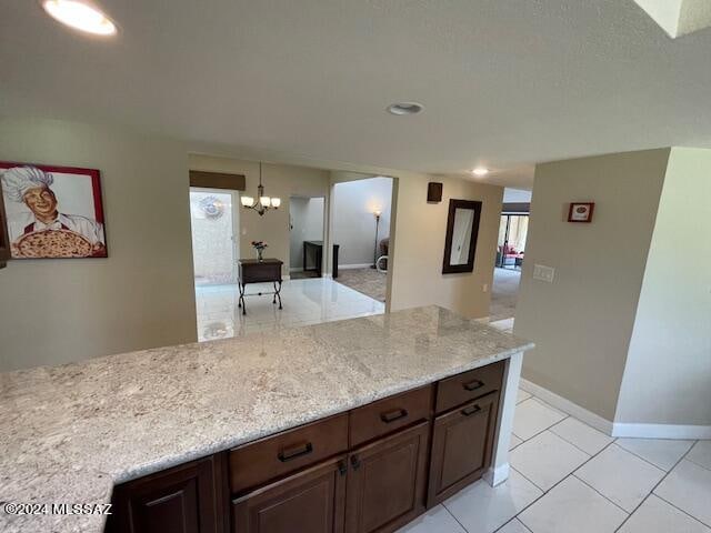 kitchen with dark brown cabinetry, light stone counters, light tile patterned floors, an inviting chandelier, and decorative light fixtures