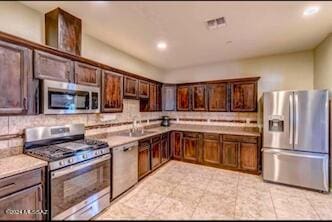 kitchen with dark brown cabinets, light tile patterned floors, sink, decorative backsplash, and appliances with stainless steel finishes