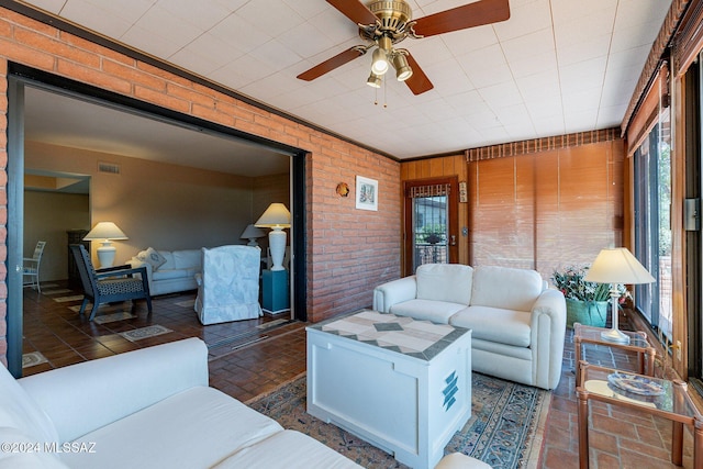 living area with ceiling fan, brick wall, brick floor, and visible vents