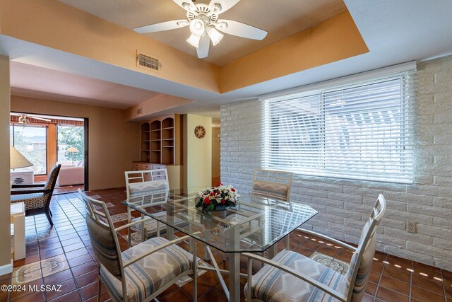 tiled dining area with ceiling fan and a raised ceiling