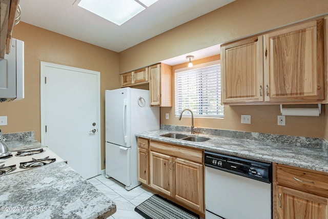 kitchen with white appliances, light brown cabinets, a skylight, and a sink