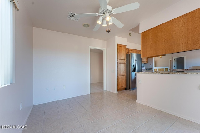 kitchen featuring ceiling fan, visible vents, light stone countertops, brown cabinetry, and stainless steel fridge