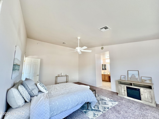 bedroom featuring light colored carpet, visible vents, a glass covered fireplace, vaulted ceiling, and ensuite bath