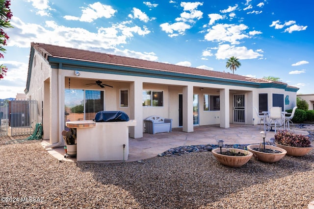 rear view of property with area for grilling, a ceiling fan, an outdoor bar, stucco siding, and a patio area