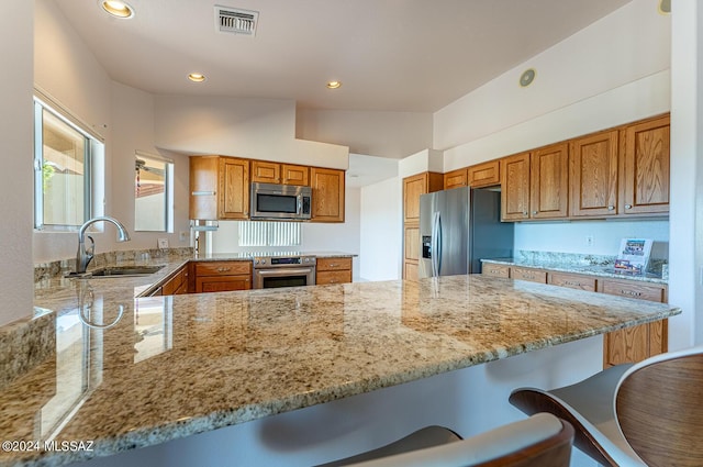 kitchen with visible vents, a peninsula, stainless steel appliances, a kitchen bar, and a sink