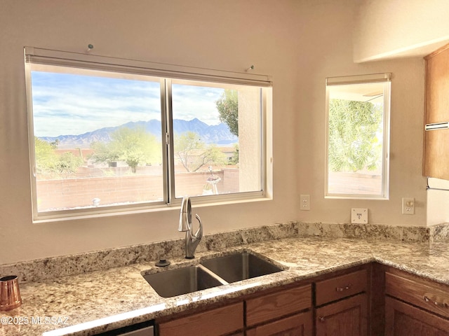 kitchen with light stone countertops, a mountain view, brown cabinetry, and a sink