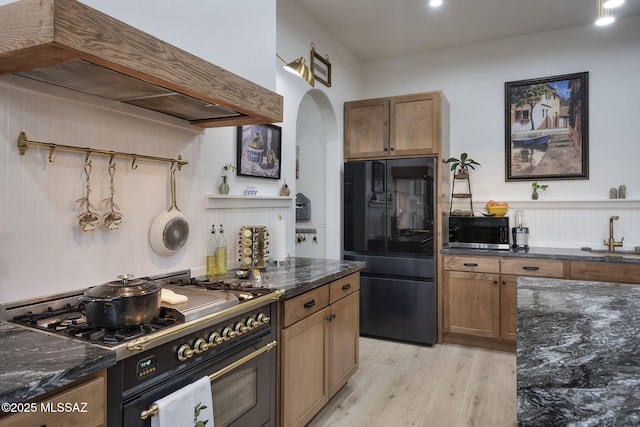 kitchen featuring black appliances, dark stone counters, brown cabinetry, and light wood-style floors