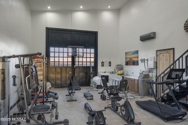 gym with a high ceiling, a wall mounted air conditioner, and washer / dryer