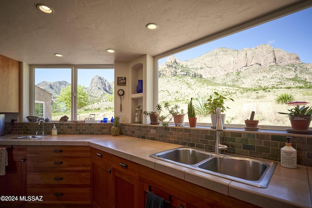 kitchen featuring a sink, decorative backsplash, a mountain view, and brown cabinets