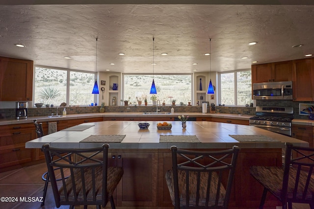 kitchen with a sink, stainless steel appliances, a breakfast bar, tile countertops, and backsplash