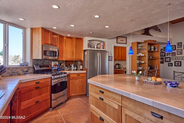 kitchen with decorative backsplash, light tile patterned flooring, hanging light fixtures, appliances with stainless steel finishes, and tile countertops