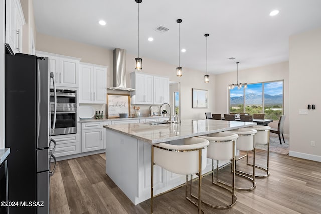 kitchen featuring a sink, visible vents, white cabinets, appliances with stainless steel finishes, and wall chimney exhaust hood