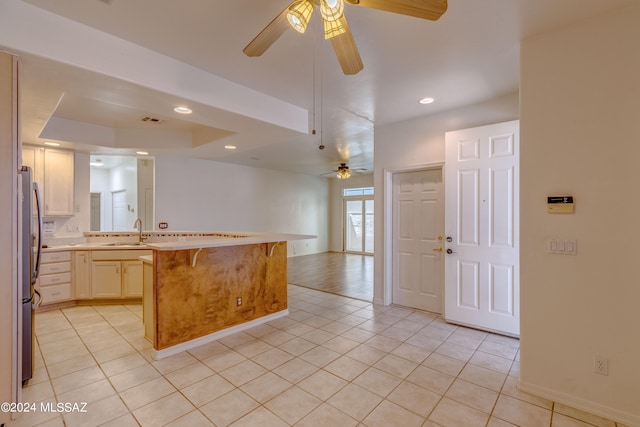 kitchen featuring ceiling fan, light tile floors, sink, a breakfast bar, and stainless steel refrigerator