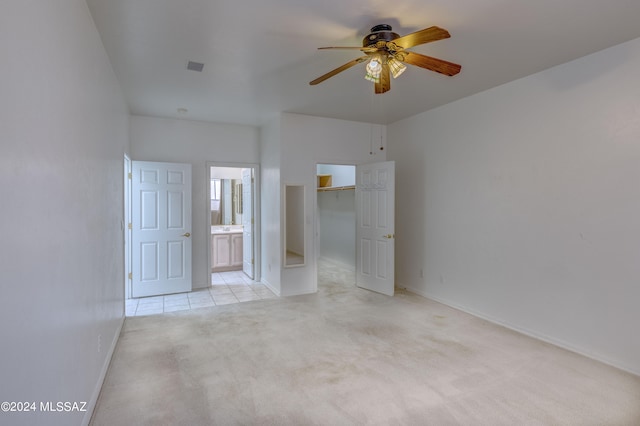 unfurnished bedroom featuring ceiling fan, a closet, light colored carpet, connected bathroom, and a walk in closet