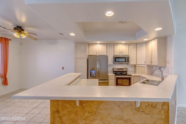 kitchen with appliances with stainless steel finishes, sink, a raised ceiling, and kitchen peninsula