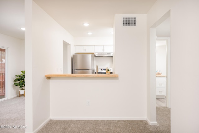 kitchen featuring stainless steel fridge, kitchen peninsula, white cabinetry, white range oven, and light colored carpet