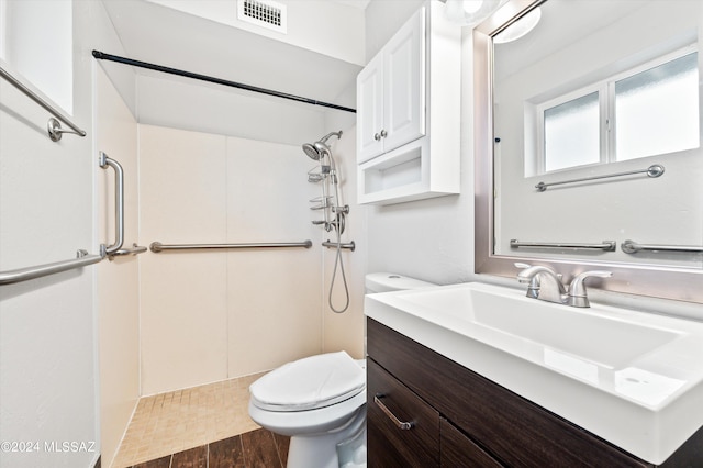 bathroom with hardwood / wood-style flooring, vanity, toilet, and a tile shower