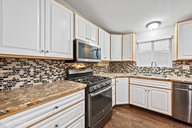 kitchen featuring appliances with stainless steel finishes, sink, backsplash, white cabinetry, and dark wood-type flooring