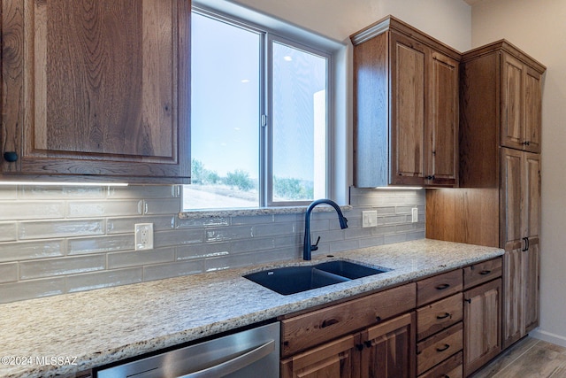 kitchen with dishwasher, backsplash, sink, light wood-type flooring, and light stone counters