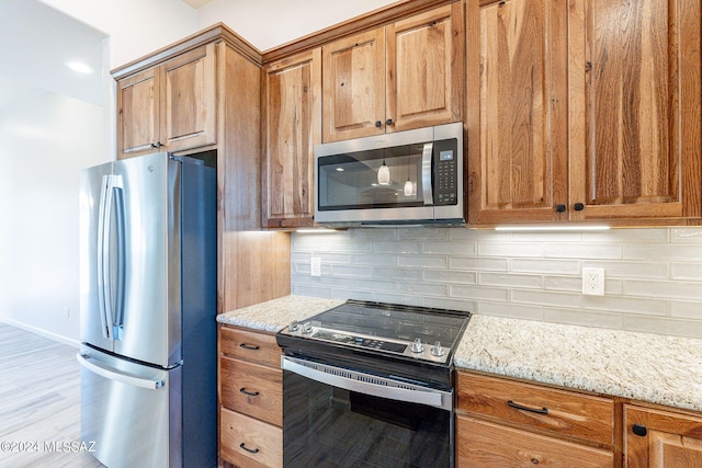 kitchen featuring decorative backsplash, light stone countertops, light wood-type flooring, and appliances with stainless steel finishes