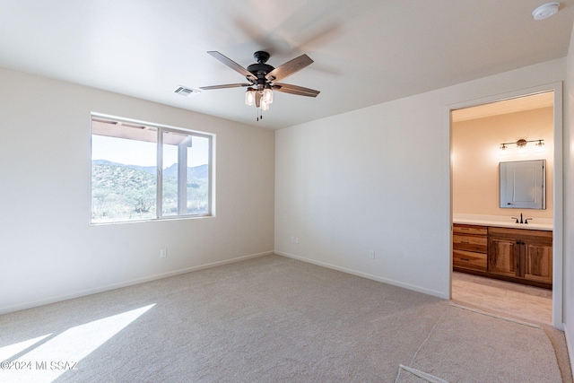 unfurnished bedroom featuring a mountain view, light carpet, sink, ceiling fan, and connected bathroom