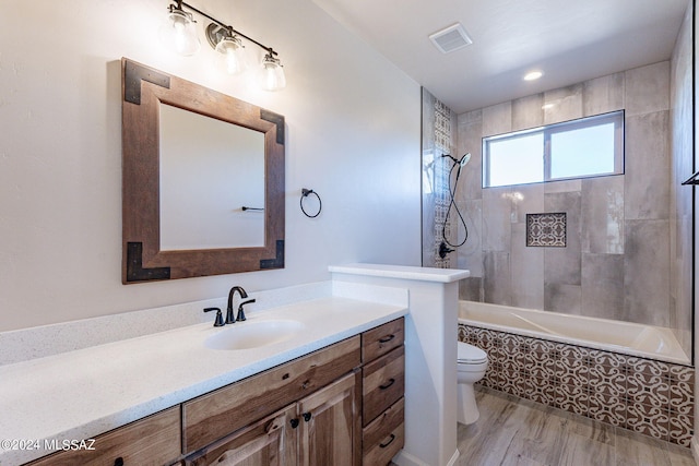 full bathroom with vanity, hardwood / wood-style floors, tiled shower / bath combo, and toilet