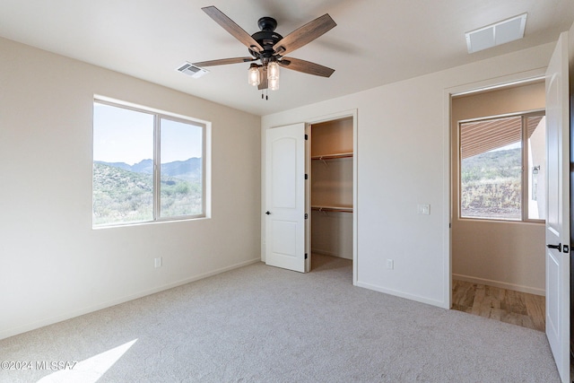 unfurnished bedroom featuring a mountain view, a walk in closet, ceiling fan, light colored carpet, and a closet