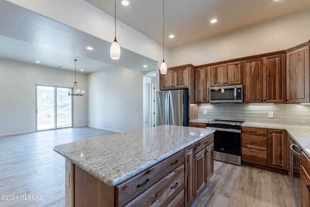 kitchen with appliances with stainless steel finishes, light stone counters, a center island, light hardwood / wood-style floors, and hanging light fixtures