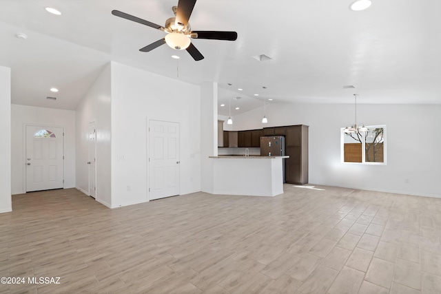 unfurnished living room with lofted ceiling, light wood-type flooring, and ceiling fan with notable chandelier