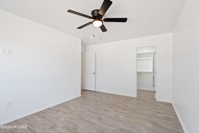 unfurnished bedroom featuring light wood-type flooring, a walk in closet, a closet, and ceiling fan