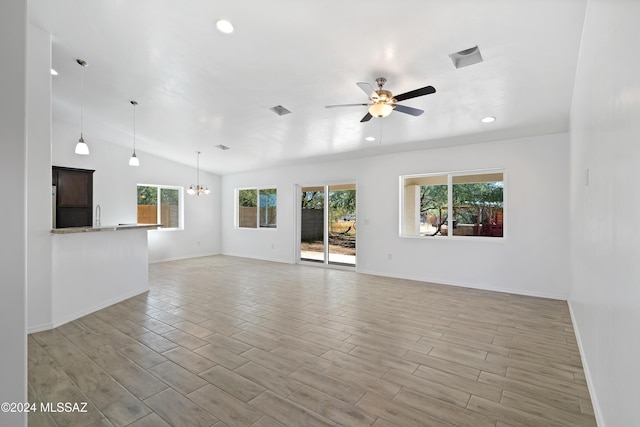 unfurnished living room with ceiling fan with notable chandelier, light hardwood / wood-style flooring, and vaulted ceiling