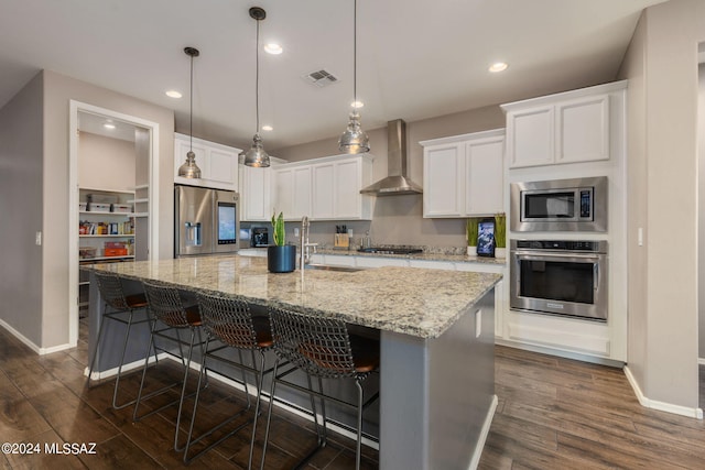 kitchen featuring appliances with stainless steel finishes, a center island with sink, wall chimney exhaust hood, white cabinetry, and dark hardwood / wood-style flooring