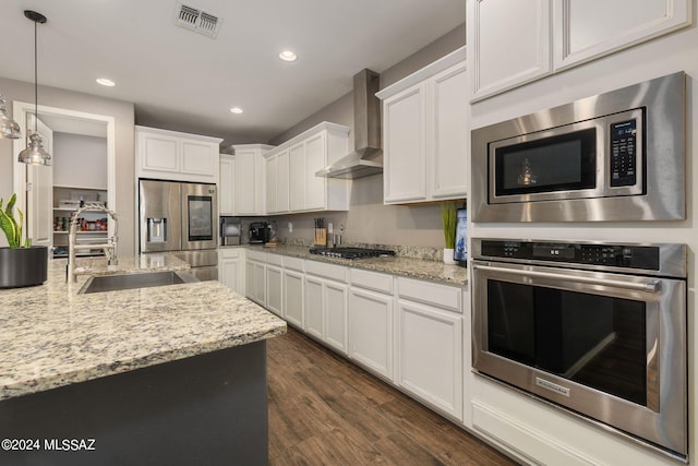 kitchen with appliances with stainless steel finishes, dark hardwood / wood-style flooring, wall chimney exhaust hood, white cabinets, and pendant lighting