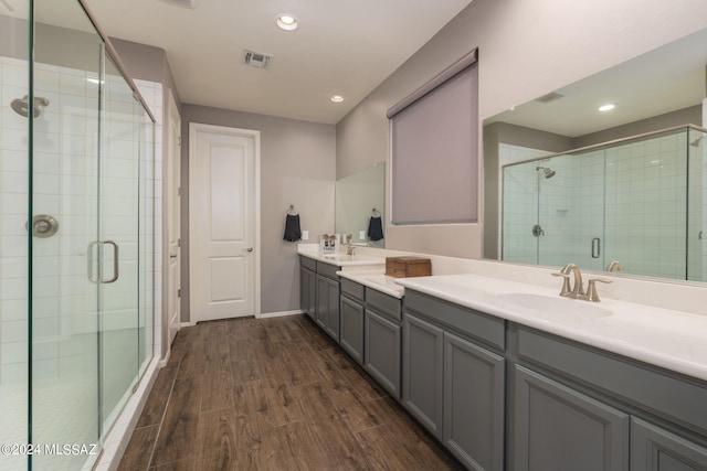 bathroom featuring hardwood / wood-style floors, double vanity, and a shower with shower door