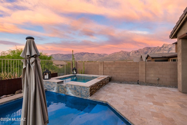 pool at dusk with a patio area, a mountain view, and an in ground hot tub