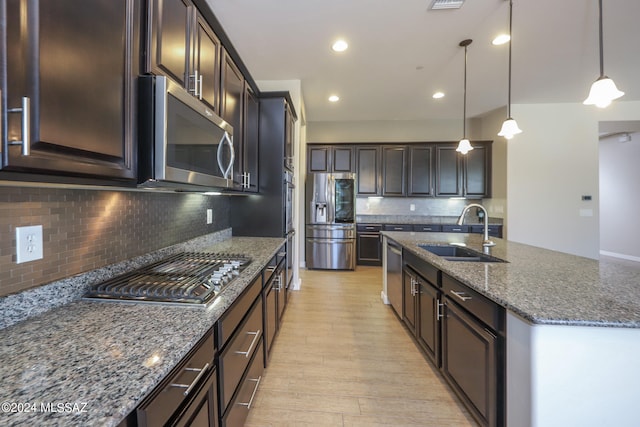 kitchen featuring stainless steel appliances, decorative backsplash, an island with sink, sink, and light hardwood / wood-style floors