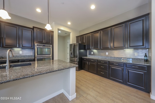 kitchen with stainless steel appliances, light hardwood / wood-style floors, backsplash, and hanging light fixtures