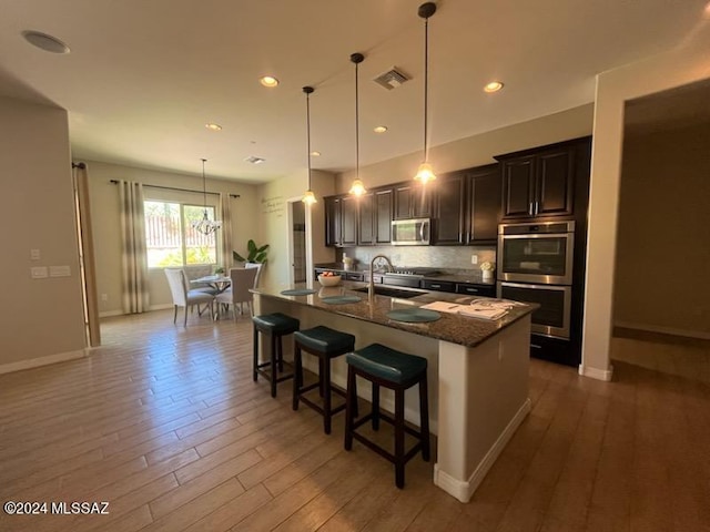 kitchen with tasteful backsplash, a kitchen breakfast bar, appliances with stainless steel finishes, wood-type flooring, and a center island with sink