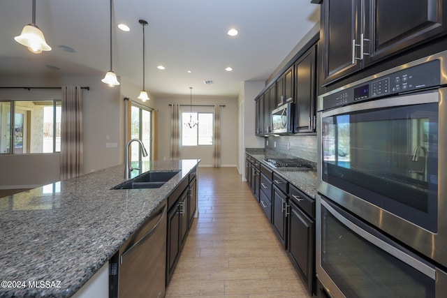 kitchen with light wood-type flooring, light stone counters, stainless steel appliances, decorative backsplash, and sink