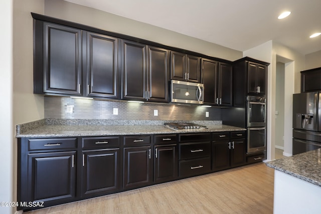 kitchen with light hardwood / wood-style floors, light stone countertops, decorative backsplash, and stainless steel appliances