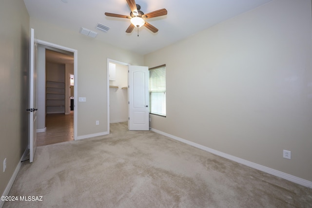 unfurnished bedroom featuring a closet, a spacious closet, light colored carpet, and ceiling fan