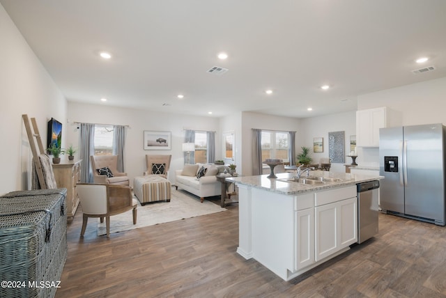 kitchen featuring wood-type flooring, stainless steel appliances, white cabinets, sink, and a center island with sink