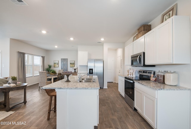 kitchen featuring appliances with stainless steel finishes, white cabinets, light stone counters, an island with sink, and dark hardwood / wood-style flooring