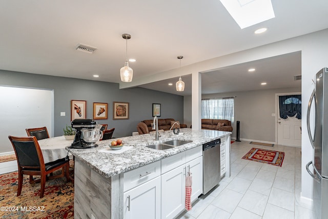 kitchen with light stone countertops, stainless steel appliances, a center island with sink, a skylight, and sink