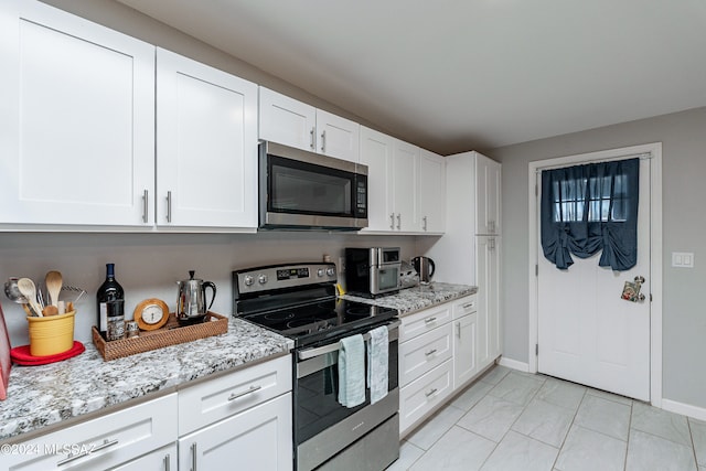 kitchen featuring white cabinetry, stainless steel appliances, light tile floors, and light stone countertops