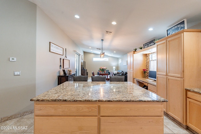 kitchen with light tile floors, a kitchen island, light brown cabinetry, decorative light fixtures, and light stone countertops