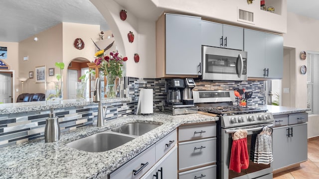 kitchen with appliances with stainless steel finishes, gray cabinets, tasteful backsplash, light stone counters, and light tile floors