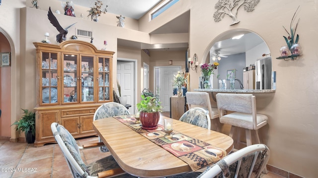 tiled dining space with ceiling fan and a high ceiling