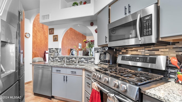 kitchen with backsplash, appliances with stainless steel finishes, sink, and light tile flooring